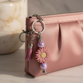 Mauve sunflower beaded keychain charm with pink tassel and iridescent lavender-purple beads clipped onto a soft elegant blush clutch purse