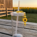 Yellow sunflower beaded straw charm on a tumbler in a rustic farm setting with sunflower field and golden hour lighting