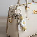 White sunflower beaded keychain charm with white tassel and iridescent yellow beads used as a zipper pull on a stylish neutral-toned purse